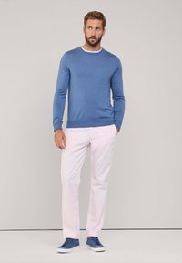 Pull en tricot bleu clair, chinos roses et baskets bleues. Le pull a un col rond, des manches ajustées et une texture douce.
