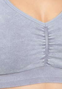 Lichtgrijze bralette met een V-hals, geplooide textuur in het midden en een geribde elastische band aan de onderkant. Zacht materiaal met een gladde afwerking.