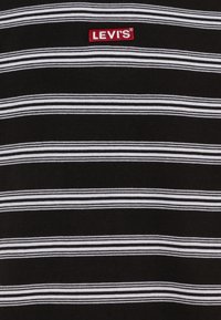 T-shirt à rayures noires et blanches avec une texture douce. Présente un logo "LEVI'S" rouge brodé centré sur la partie supérieure de la poitrine.