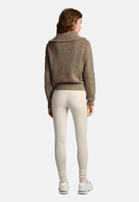 Brązowy sweter z dzianiny z kołnierzem typu cowl, ribbowym wykończeniem u dołu i rękawami; w połączeniu z jasnymi legginsami i białymi sneakersami.