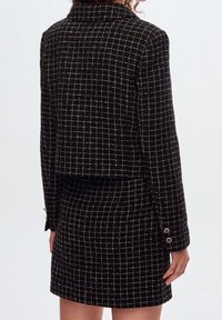 Zwart-wit geruite rokkenpak met een cropped jasje, voorzien van een kraag met inkeping en goudkleurige knopen op de mouwen.