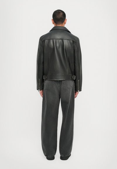 Μαύρο δερμάτινο μπουφάν μοτοσικλέτας με φαρδύ γιακά, πλάγιες πόρπες και μανίκια με φερμουάρ. Συνδυασμένο με φαρδιά, σκούρα γκρι τζιν.