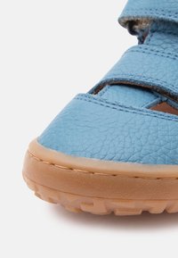 Κοντινή εικόνα μπλε δερμάτινου σανδαλιού με ρυθμιζόμενο λουράκι και υφασμένη, ανοιχτό καφέ, λαστιχένια σόλα.