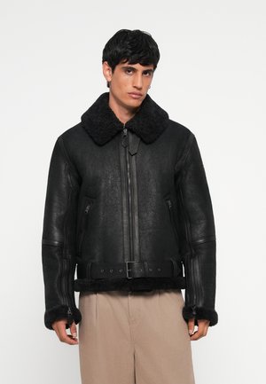 Black leather jacket with a faux fur collar and cuffs, zippered front, and belted waist; features a textured finish and practical side pockets.