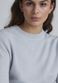 Lyseblå, sweater med rund hals lavet af blødt strikmateriale; har ribbet halsåbning og subtil tekstur, uden markante mønstre eller accenter.