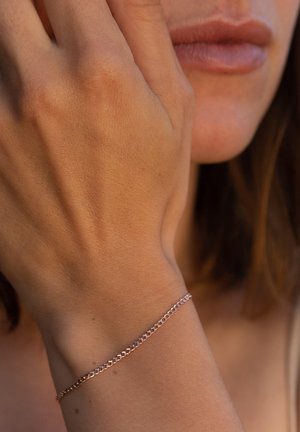 Roségoldene Kettenarmband an einem Handgelenk, mit ineinandergreifenden Gliedern und glatter Oberfläche, vor einem gebräunten Hautton.