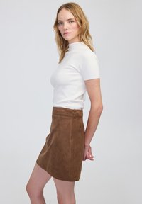 Top blanco de manga corta combinado con una falda mini de pana marrón que presenta un patrón texturizado y un bolsillo trasero.