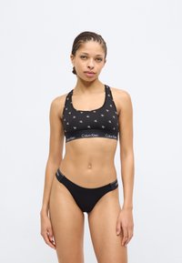 Μαύρο αθλητικό σουτιέν με επαναλαμβανόμενο μοτίβο λογότυπου CK, με τετράγωνη λαιμόκοψη και φαρδιές τιράντες. Μαύρο σλιπ χαμηλής μέσης με λωρίδα μέσης με λογότυπο.