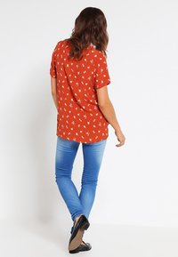 Rode bloemen korte mouwen top van een lichtgewicht stof, gecombineerd met strakke blauwe jeans. De top heeft een subtiel patroon en een ontspannen pasvorm.