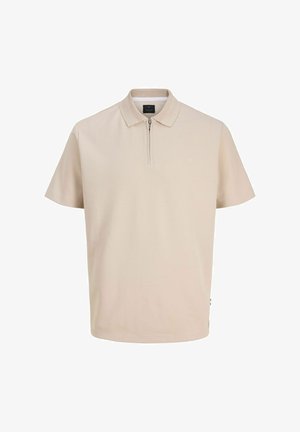 Bež polo majica s kratkimi rokavi, z njeno teksturirano ovratnico in polovično zadrgo na sredini spredaj.