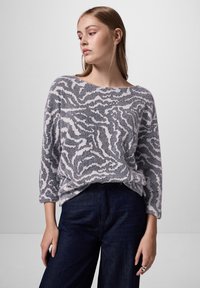 Leichter, grau-weißer Strickpullover mit Wellenmuster, weitem Halsausschnitt und Dreiviertelärmeln, kombiniert mit einer dunklen Jeans.