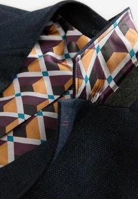 Marineblauwe textuurstof met een contrasterende geometrische voering in paars, goud, zwart en teal. Opvallende afwerkingdetails zichtbaar.
