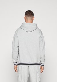 Šedá mikina s kapucňou a voľným strihom, široké manžety a pruhovaný pás. Mäkko jemný materiál, minimalistický dizajn, žiadne viditeľné logá.