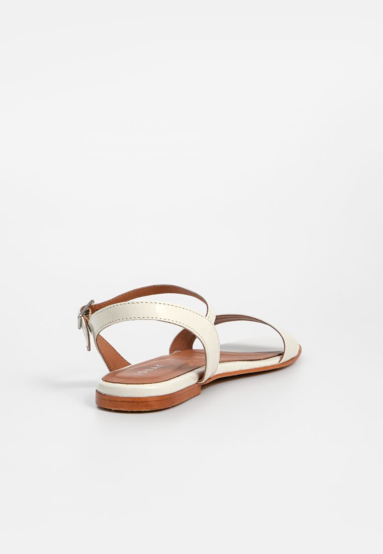 Sandalia de cuero blanco con plantilla marrón, que presenta dos correas curvas y una correa trasera con hebilla. Textura suave, suela plana.
