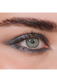 Nära bild av ett öga med grå-blå iris, mörk eyeliner och välmarkerade ögonfransar. Huden runt ögat är slät och lätt strukturerad.