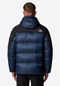 Niebieska i czarna kurtka puchowa z kapturem, z pikowanym wzorem, błyszcząca tekstura oraz logo na górnej części pleców.