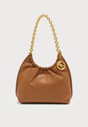 Sac à main en cuir marron avec une bandoulière en chaîne dorée et un pendentif rond en or avec le logo Michael Kors sur le côté.
