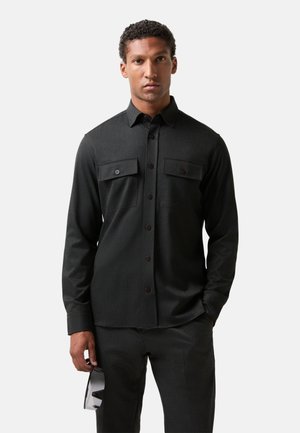 Donkergrijze langekleurige shirt met twee borstzakken, knoopsluiting aan de voorkant en textielstof. Gestyled met bijpassende broek en zonnebril.