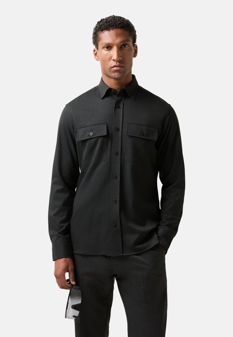 Dark grey long-sleeve shirt with two chest pockets, button-up front, and textured fabric. Styled with matching pants and sunglasses.