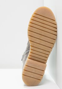 Harmaa mokkanahkainen lenkkitossu, jossa on pintakuvioitu, tan-värinen kumipohja. Kuosisuunnitelmassa on raidallinen kuvio ja pieni etiketti, jossa on koko 37 lähellä kantapäätä.