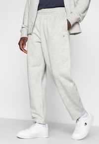 Γκρι παντελόνι φόρμας από απαλό βαμβακερό μείγμα, με ελαστική μέση, πλαϊνές τσέπες και στενά μπατζάκια, συνδυασμένο με λευκά αθλητικά παπούτσια.