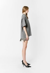 Camisa gris oversized de manga corta, con textura lisa y lazos laterales, combinada con pantalones cortos de estampado y zapatos de tacón negros.
