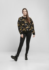Zwarte trui met een patroon van gouden rendieren en witte sneeuwvlokken, gecombineerd met zwarte slim-fit broeken en glanzende zwarte combat boots.