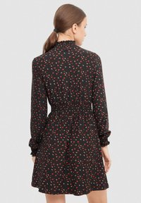 Vestido negro con estampado de flores rojas, escote fruncido, mangas largas con puños recogidos y un corte holgado en la cintura.