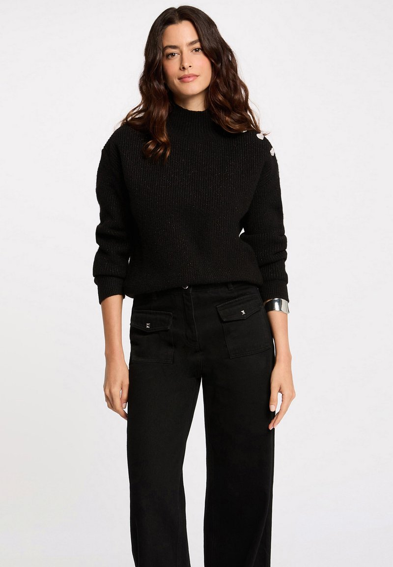 Jersey negro de punto con un cuello alto y textura acanalada, combinado con pantalones negros de cintura alta que cuentan con bolsillos delanteros y acentos plateados.