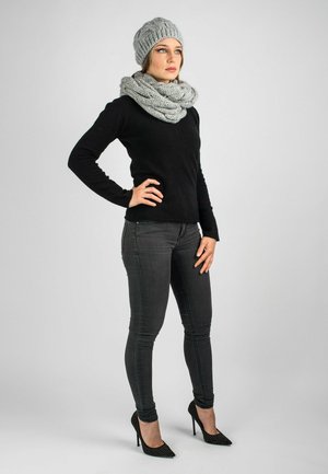 Berretto di lana grigio e sciarpa abbinati a un maglione nero e jeans scuri. Scarpe col tacco nere presentano un motivo borchiato.