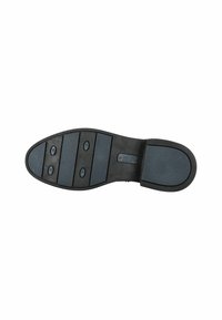 Suela de un zapato de vestir negro con secciones de goma antideslizante azul y pequeños clavos circulares sobre un fondo blanco.