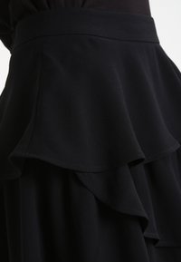 Svart stuvskjol med en volangdesign, tillverkad av mjukt tyg. Har ett slätt midjeband och lager av volanger längs kanten.