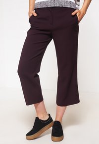 Burgundyfärgade avkortade byxor med sidofickor och en avsmalnande bendesign, i kombination med svarta platåskor med nitar.