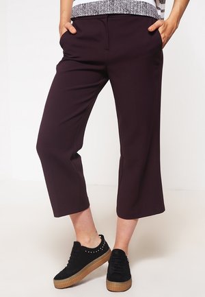 Pantalons cropped bordeaux avec poches latérales et une coupe fuselée, associés à des baskets compensees noires avec des accents cloutés.