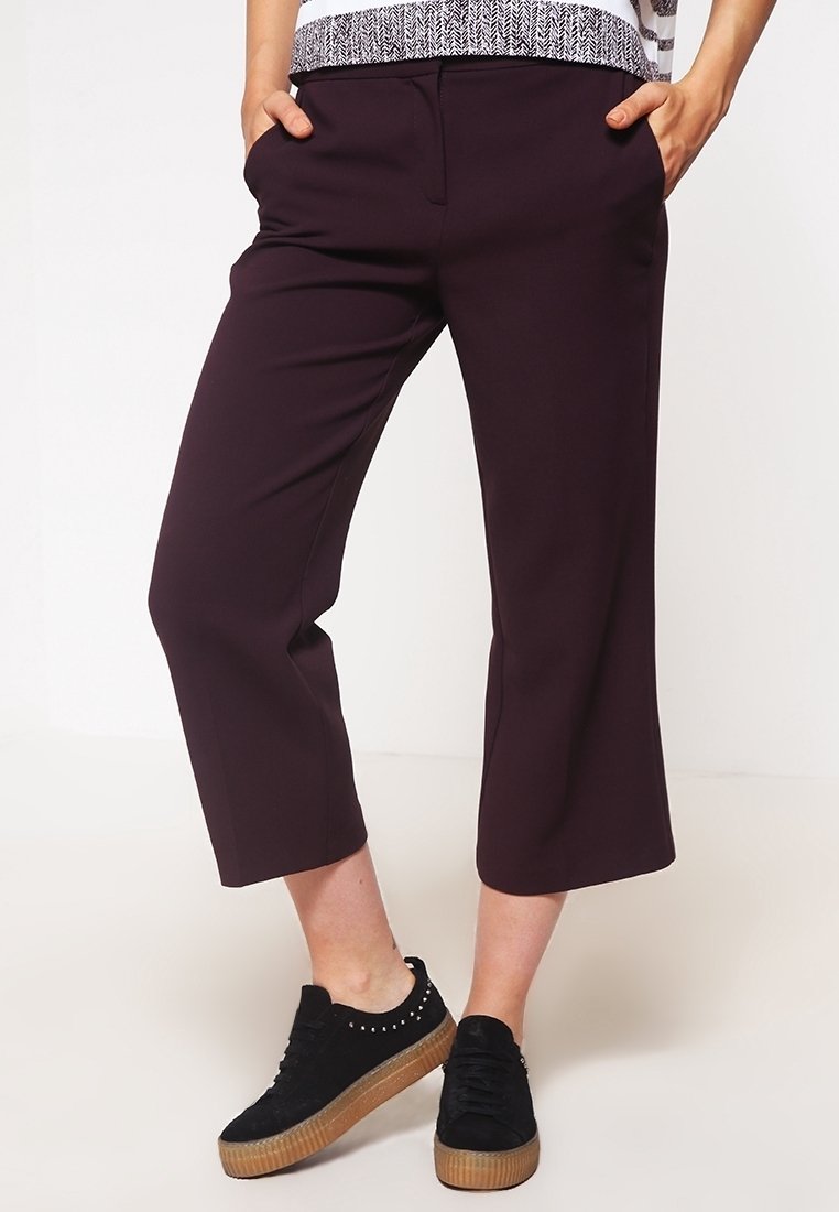 Burgundyfärgade avkortade byxor med sidofickor och en avsmalnande bendesign, i kombination med svarta platåskor med nitar.