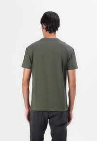 Olijfgroen T-shirt met korte mouwen van zacht materiaal, voorzien van een ronde hals en een rechte zoom, weergegeven vanuit de achterkant.