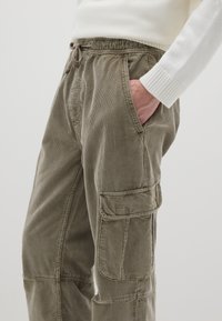 Corduroy cargobroek in olijfgroen, met een elastische tailleband, zijzakken en een gestructureerd geribd patroon.