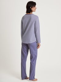 Gestreiftes Langarmshirt mit rundem Ausschnitt, kombiniert mit einfarbigen helllila Hosen. Die Materialien wirken weich und lässig.