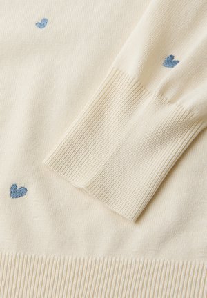 Manche de pull en maille crème avec poignet côtelé et petits cœurs bleus brodés dispersés sur le tissu.