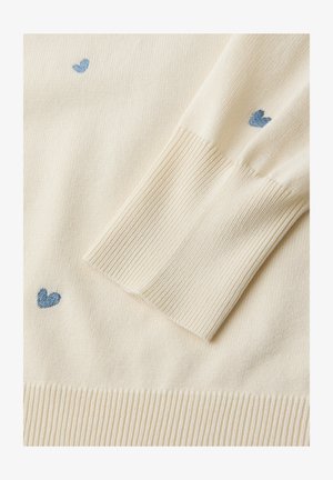 Rękaw kremowego swetra z dzianiny, z prążkowanym mankietem i małymi, haftowanymi na niebiesko sercami rozsianymi po tkaninie.