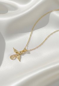Guldkæde med en vedhæng formet som en fugl, med delikate vinger og en glitrende detalje. Stiller sig mod glat, hvidt stof.
