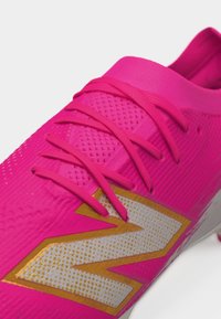 Scarpa da calcio rosa acceso con tomaia testurizzata, lacci rosa abbinati e grande logo bianco contornato d'oro sul lato.