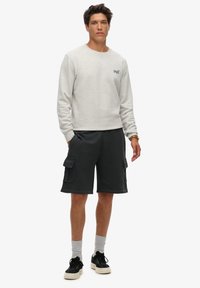 Sudadera gris claro con cuello redondo y un logo pequeño; pantalones cortos cargo negros con bolsillos laterales; zapatos negros; calcetines grises.