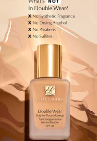 Podkład Estee Lauder Double Wear w beżowej szklanej butelce z złotą zakrętką. Tło przedstawia miękki, abstrakcyjny wzór w ciepłych odcieniach.
