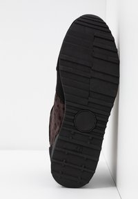 Semelle en caoutchouc noir avec grip texturé, présentée avec un dessus en daim à motif léopard marron. Accentuée par un panneau latéral noir lisse.