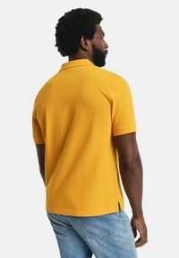 Kurzarm-Polohemd aus leuchtend gelbem Stoff, mit klassischem Kragen, seitlichen Schlitzen und glatter Textur. Trägt man mit Jeans.