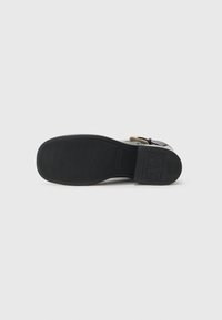 Suela de zapato de goma negra con superficie texturizada. Presenta una impresión de logo y forma redondeada. Diseño minimalista sin patrones ni acentos visibles.