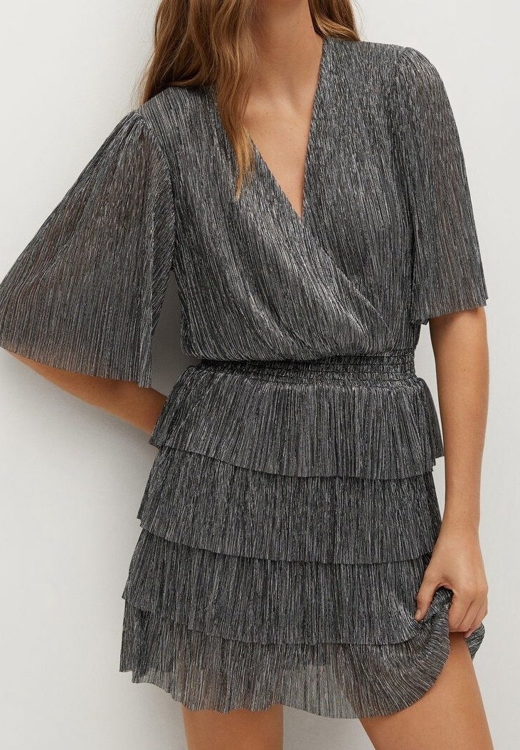 Femme portant une robe plissée gris argenté avec manches courtes volantées, un col croisé, une taille cintrée et une jupe à volants à étages.
