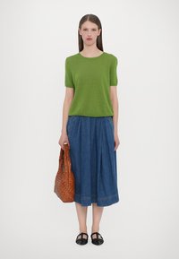 Groene korte mouwen trui, denim geplooide midi rok, gevlochten bruine tas en zwarte schoenen. Eenvoudig ontwerp, zachte texturen en complementaire kleuren.