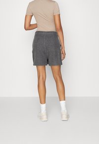 Persona in piedi di spalle con un top beige a maniche corte, pantaloni corti grigi a vita alta, calzini bianchi e sneakers bianche.